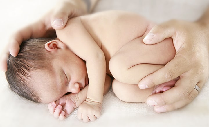 Recién nacido en posición fetal recogido manos padre