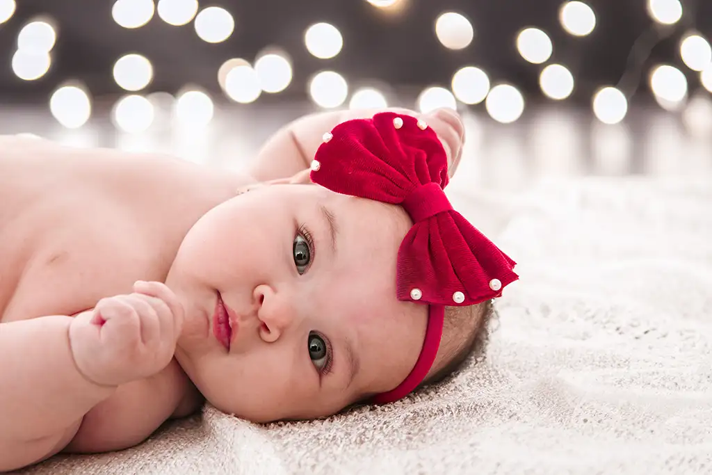 Bebé con decoración navideña de luces y diadema de lazo rojo navideño