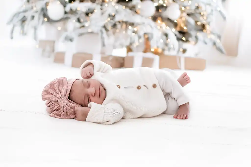 Bebé recién nacido en una fotografía navideña, acompañado de un árbol de Navidad en un escenario elegante y personalizado.