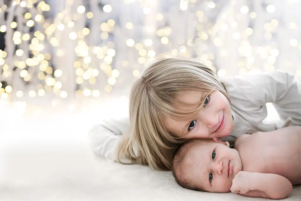 Fotografía navideña de un niño y un bebé recién nacido, fondo luces