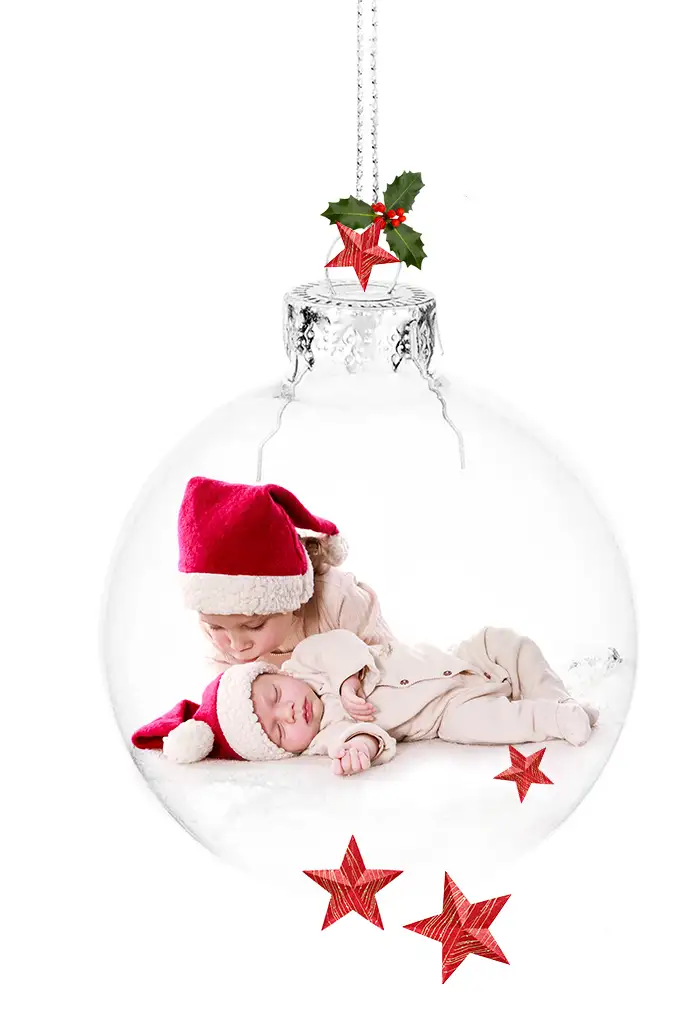 Bebé recién nacido junto a hermano besándolo en el interior de una bola de cristal navideña